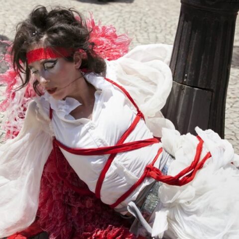 Artist in performance wearing a white dress covered in red bands