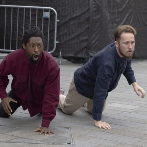 Two people on a concrete floor reacting to something off camera