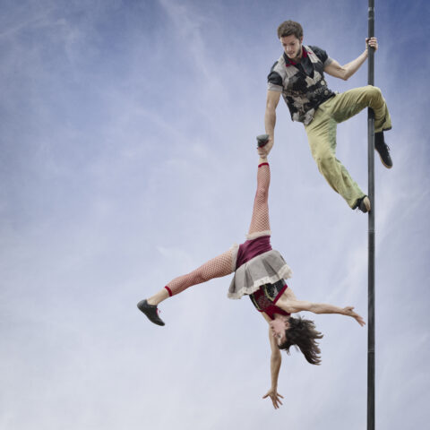 man hung from a pole holding a woman by her ankles