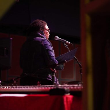 A woman reading into a mic at the Drill House
