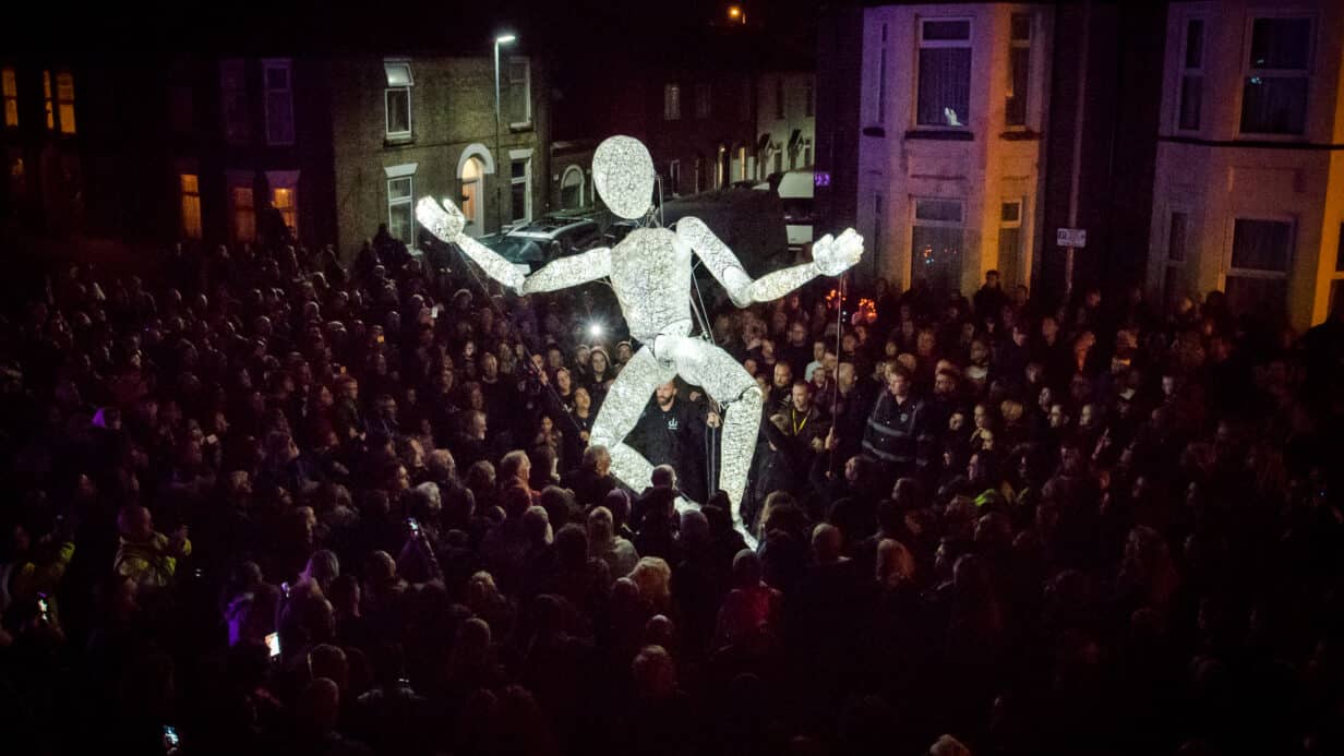 An illuminated puppet surrounded by a big crowd in a dark night.