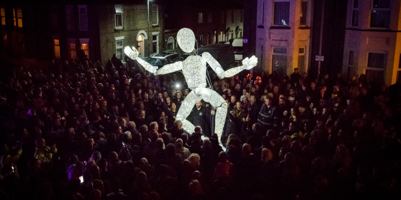 An illuminated puppet surrounded by a big crowd in a dark night.