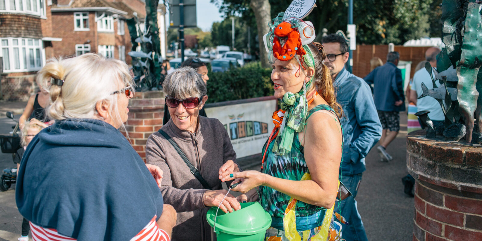 Festival attendees placing money in a donation bucket while talking to event staff