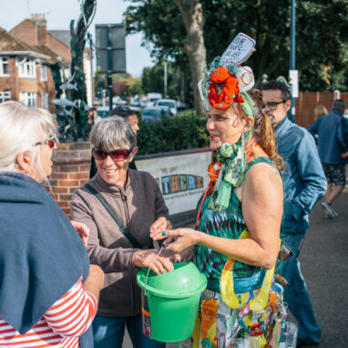 Festival attendees placing money in a donation bucket while talking to event staff