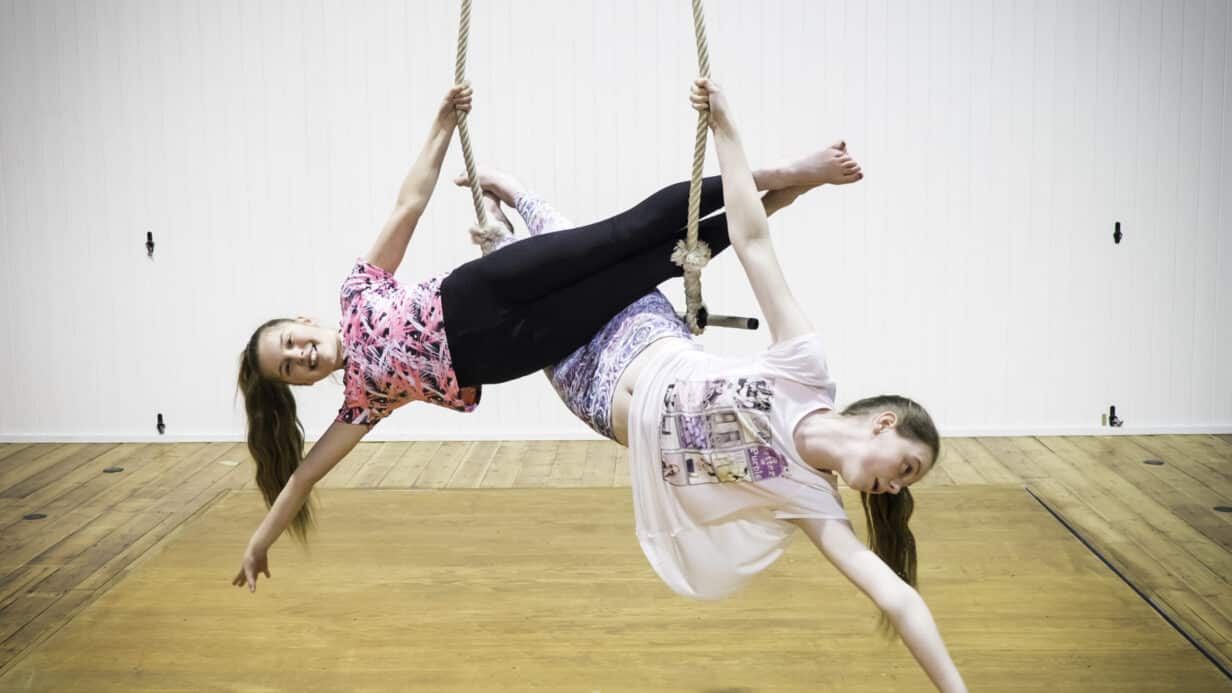 Two girls hang off a bar attached to ropes at the Drill House
