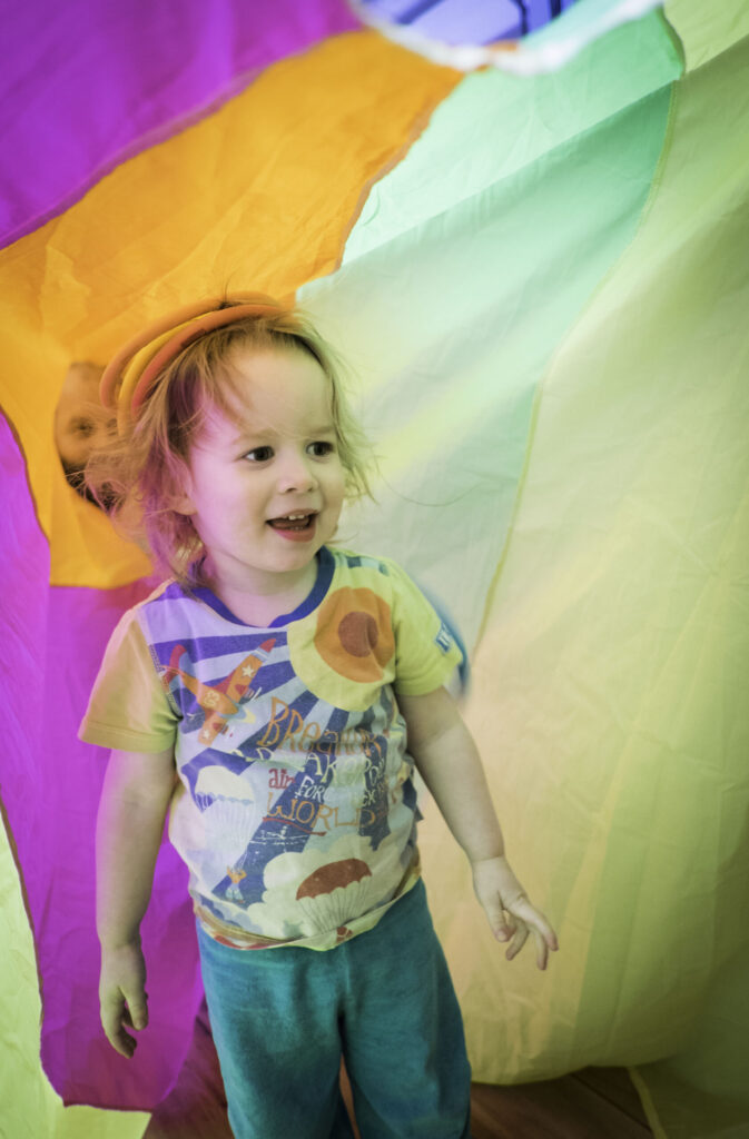 Child enjoying circus session surrounded by coloured parachute