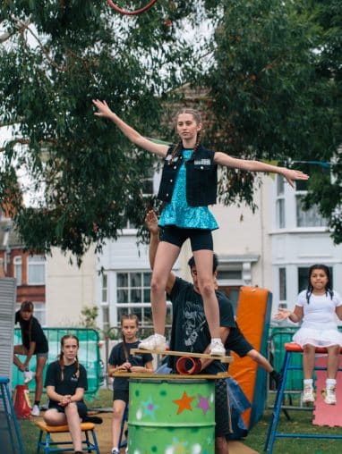 Girl balances on a rola bola on top of a barrel