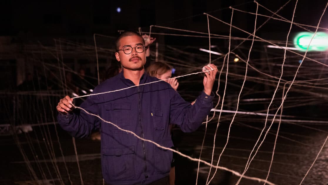 Person holding some yarn as it has been strewn across a public space behind them in a constricting pattern