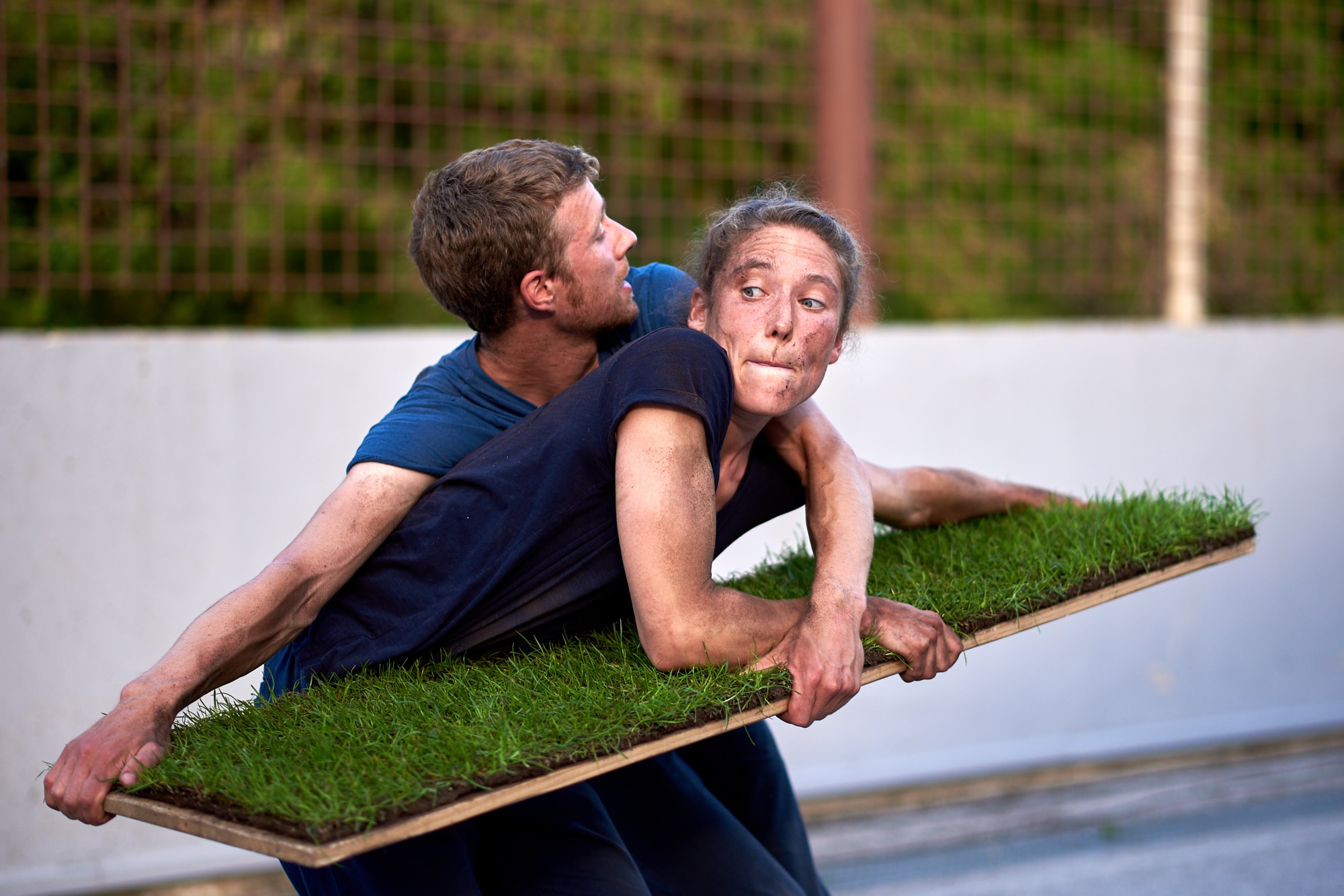 Performance of Grasshoppers. Two performers holding a plank of wood with turf grass laid on top. They contorted around each other