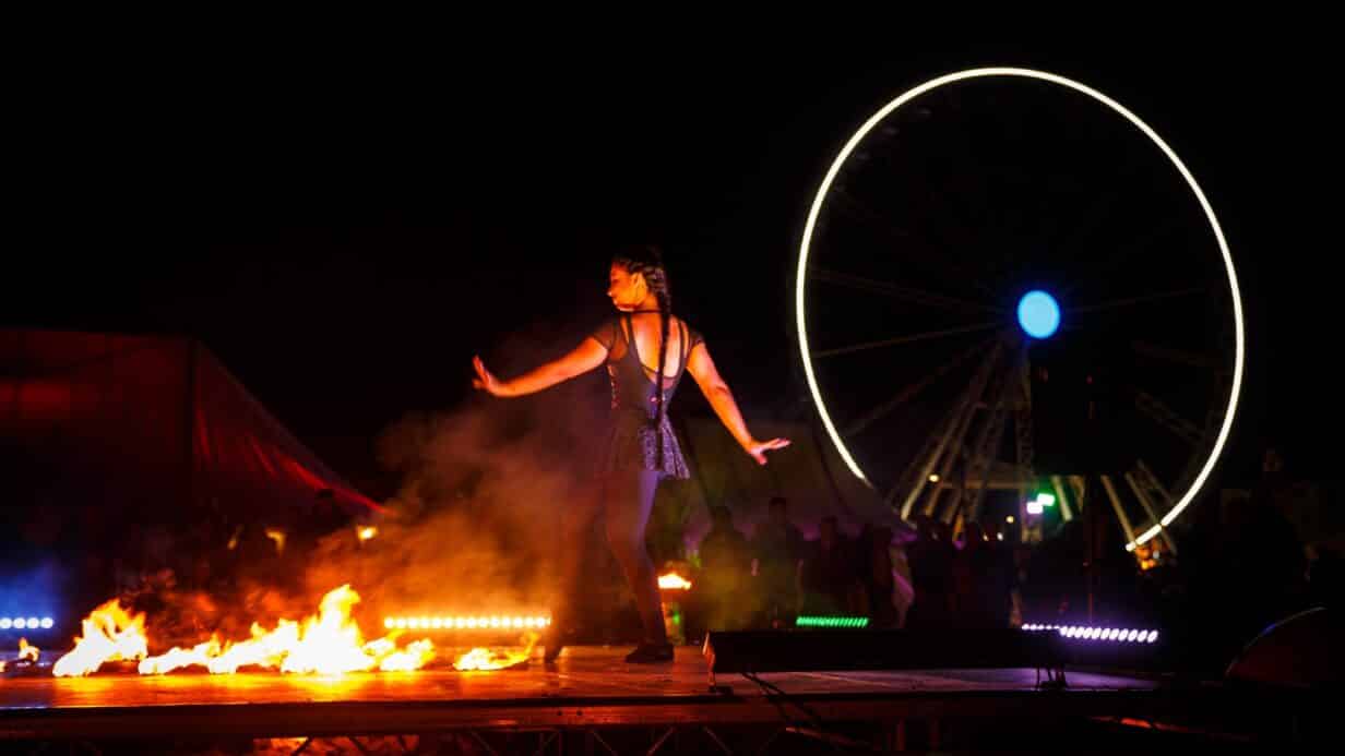 A performer performing on a stage of fire with the Great Yarmouth ferris wheel in the background