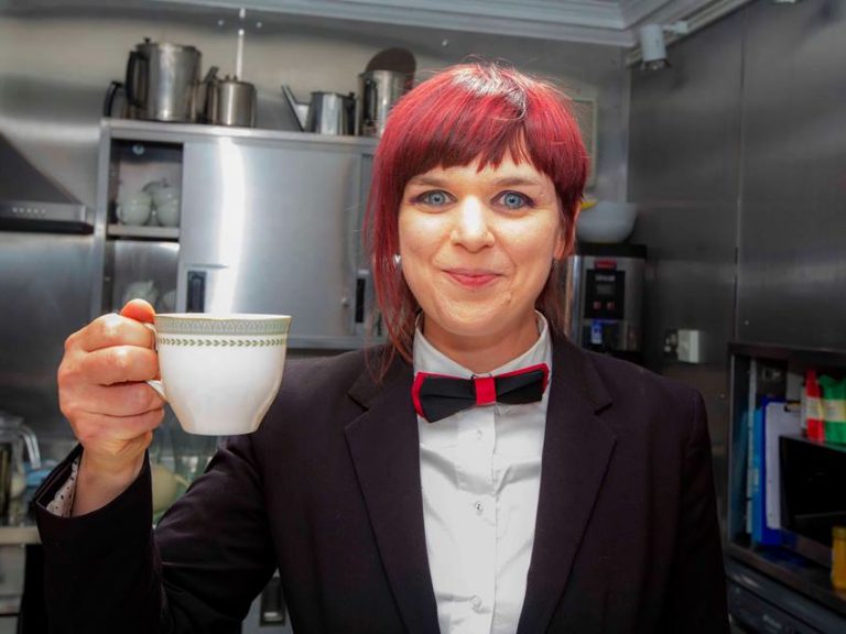 Posh Club wearing a swanky suit and raising a cup of tea