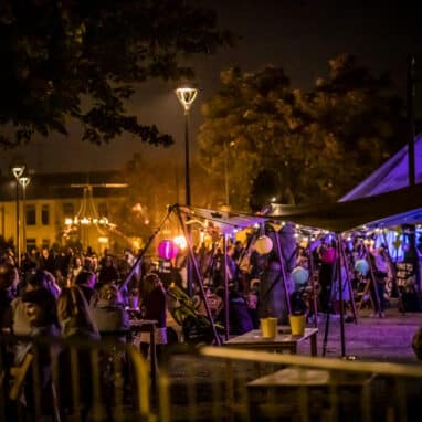 An atmospheric image of a park bar with lights and people enjoying a drink at the Out There Festival