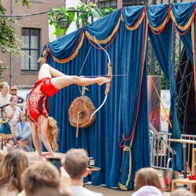 A performer in a handstand, firing a bow and arrow with their feet