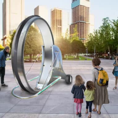 An Audience looks on at a large art piece shaped like a Wheel