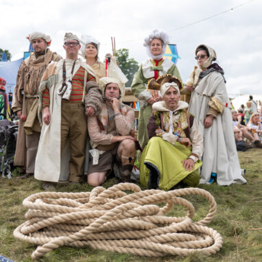 A group of performers stand in costume behind a pile of rope