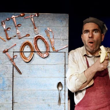 A performer eating a banana in front of a set with the name 