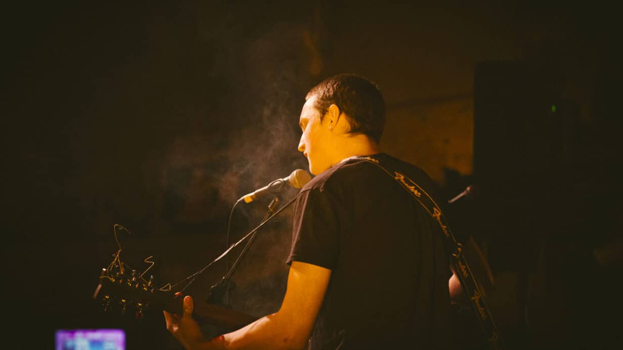 A person playing acoustic guitar in a dark room, creating soothing melodies with passion and skill.
