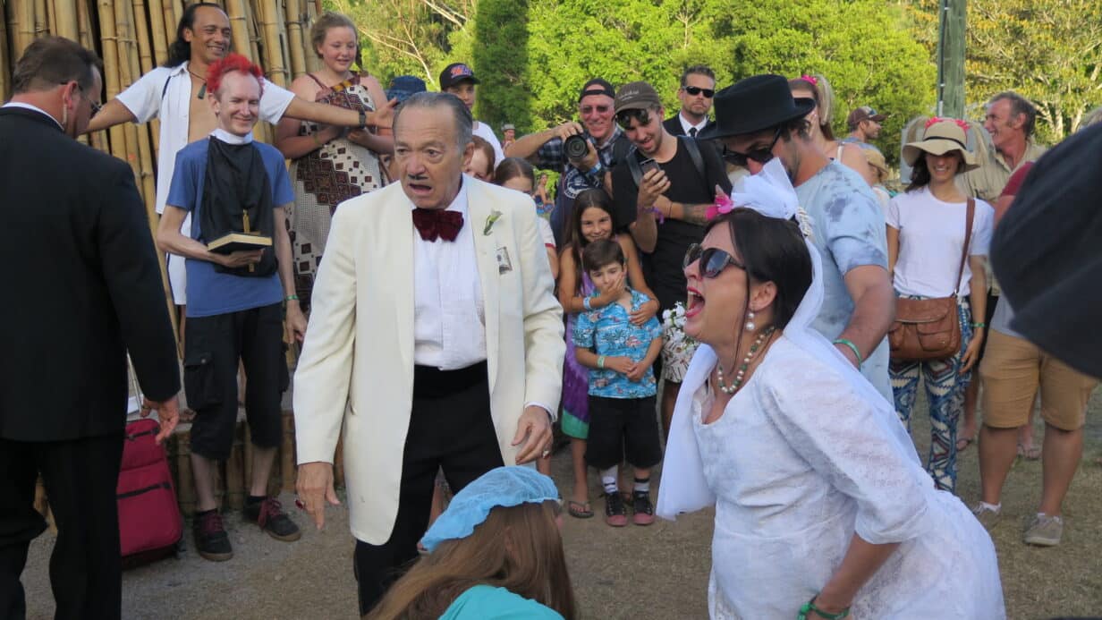 A woman dressed in a brides outfit, yelling next to a man dressed in a white tuxedo like a mafiaoso