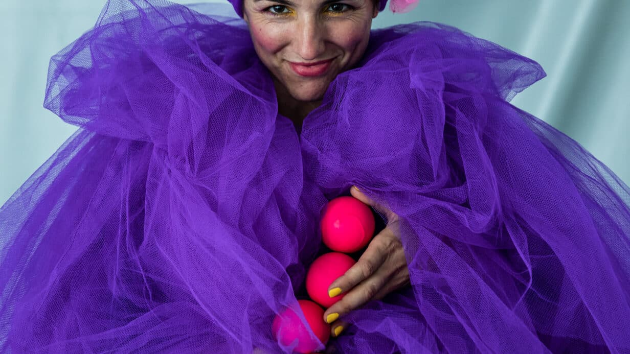 Juggler dressed in a bright purple cloud dress smiles at the camera