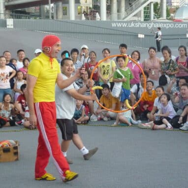 A man dressed in bright yellow and red and another man holding a hula hoop