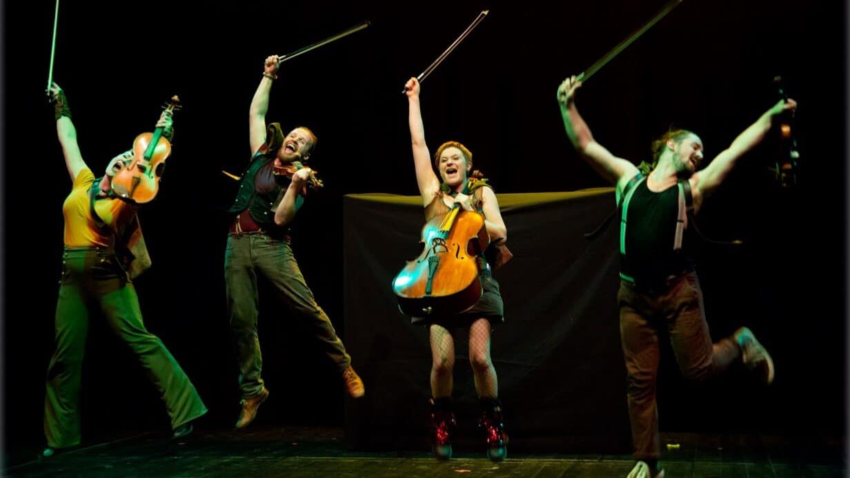 4 people jumping for joy holding violins on stage