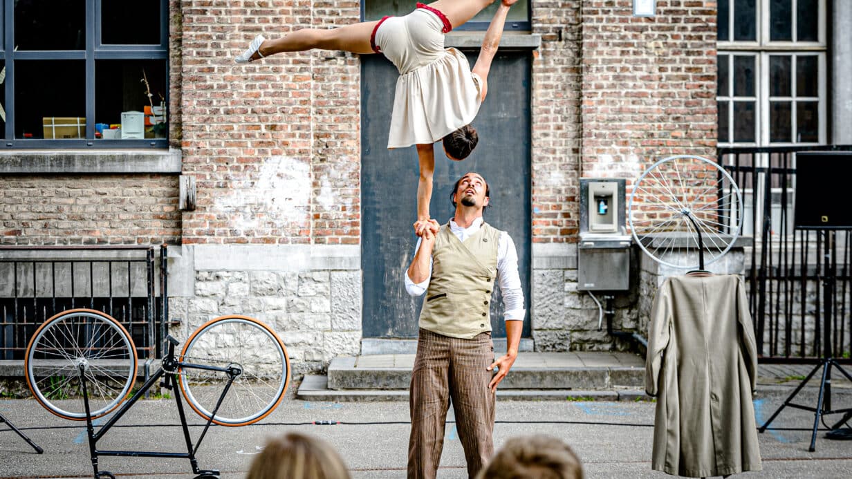 Two acrobatics perform a one hand balance in the street