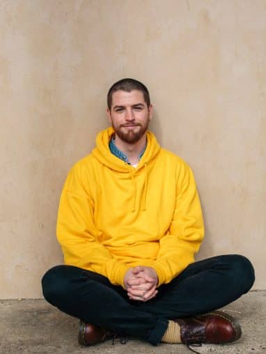 A man with a shaved head in yellow hoodie