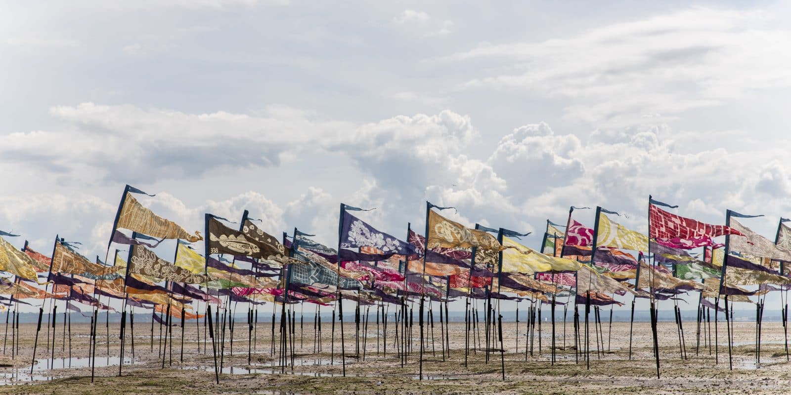 Hundreds of colourful flags planted on a beach as the tide comes in for Beach of Dreams