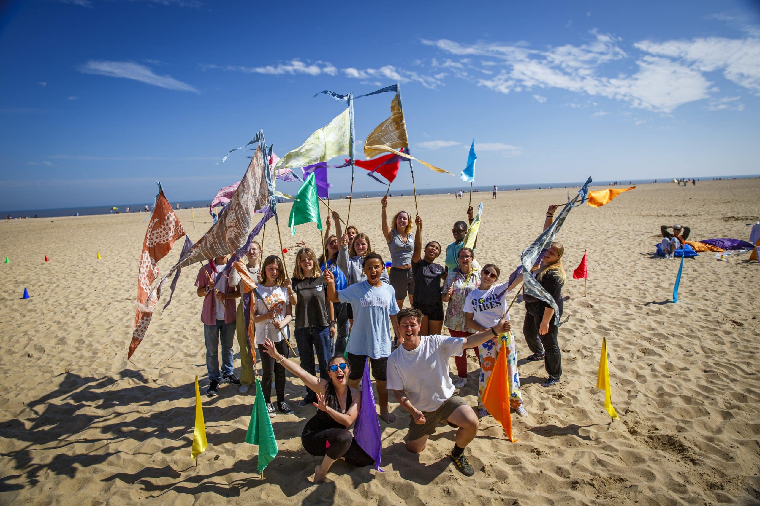 People stood on a beach waving brightly coloured flags