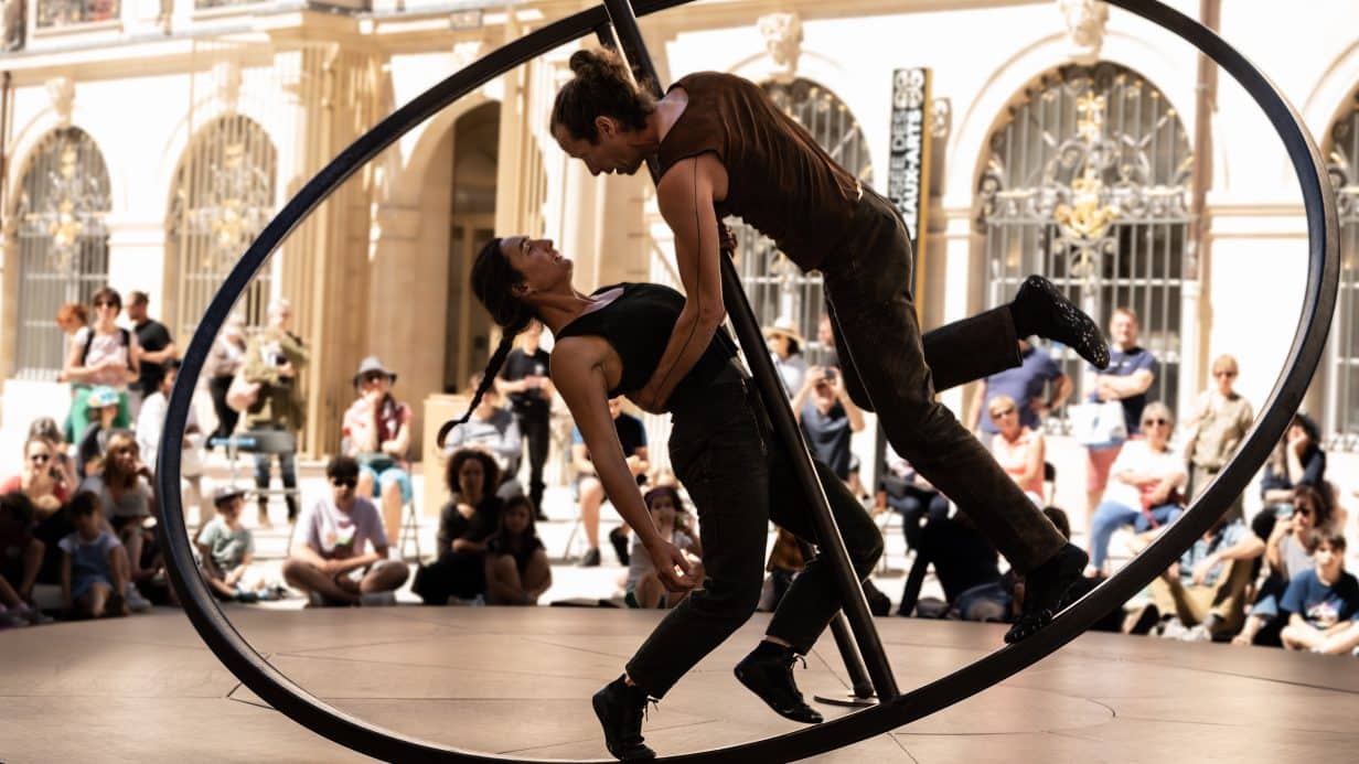 Two circus performers balancing on a wheel