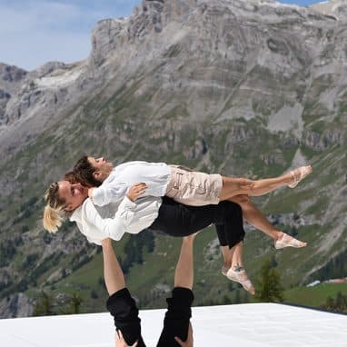 Person balancing two people on their feet in front of mountains