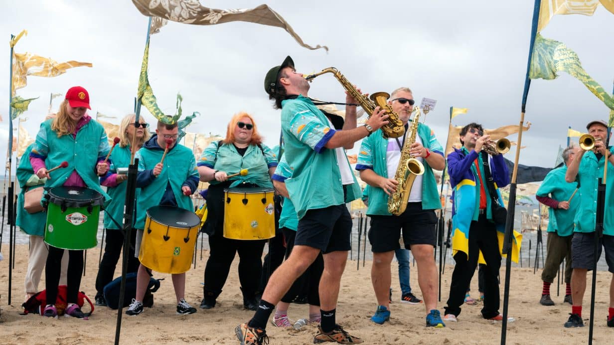 Beach of Dreams – Morecambe Person playing saxophone in front of lots of flags